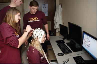 Researchers, clad in a UMD t-shirts, placing an EEG device on a person's head