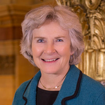 A woman with short hair, smiling, and wearing a blue coat