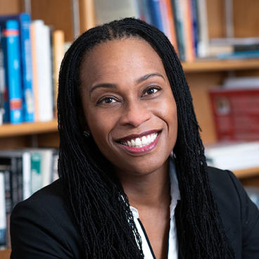 A lady smiling, wearing black coat, with her hair braided